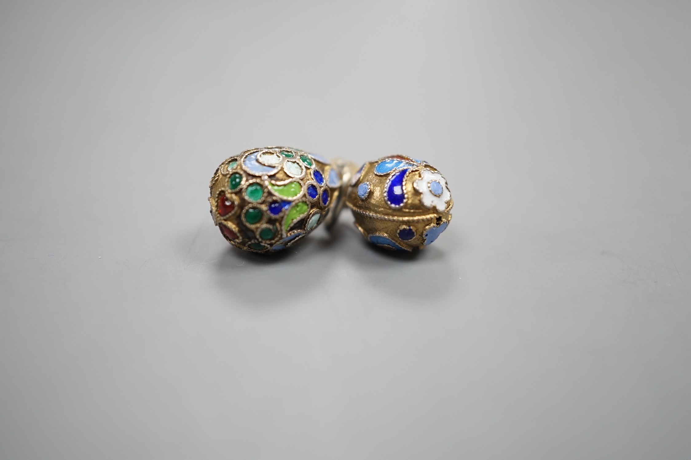 An early 20th century Russian 84 zolotnik and polychrome cloisonné enamel set egg pendant, maker's mark HT?, 17mm and a similar smaller egg pendant, maker's mark HM?.